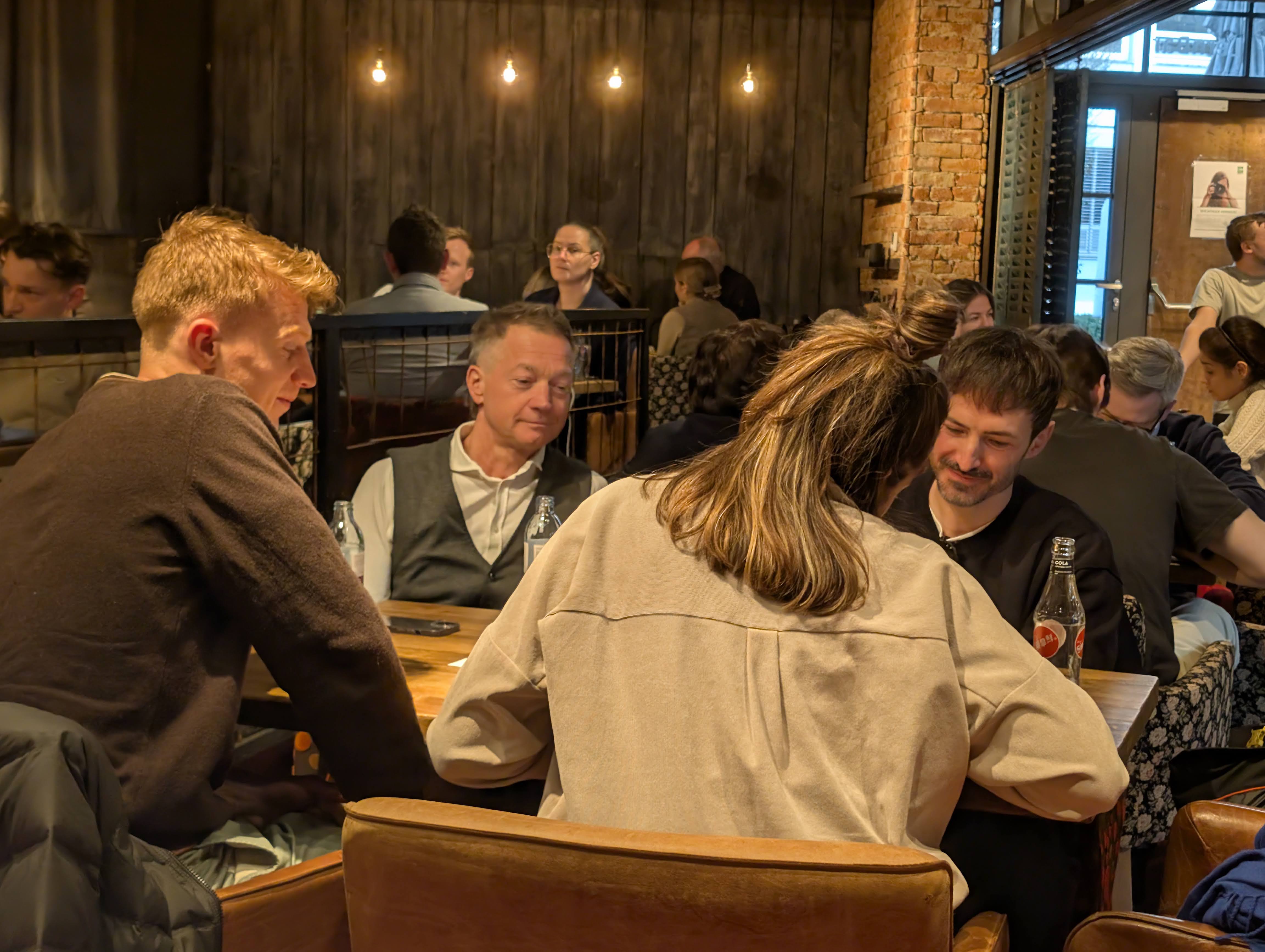 Buildathon #2 — Tischrunde im warmen Licht, Köpfe über Laptops