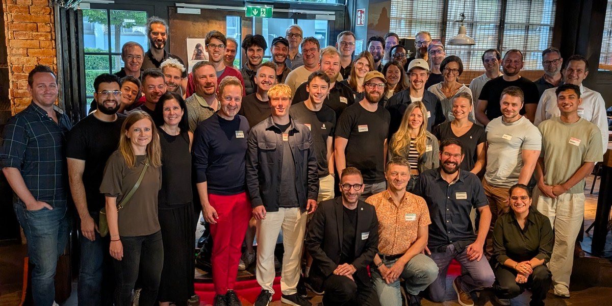 Rund fünfzig Menschen stehen dicht gedrängt für ein Gruppenfoto in einem Lokal, vorne knien einige, alle blicken in die Kamera