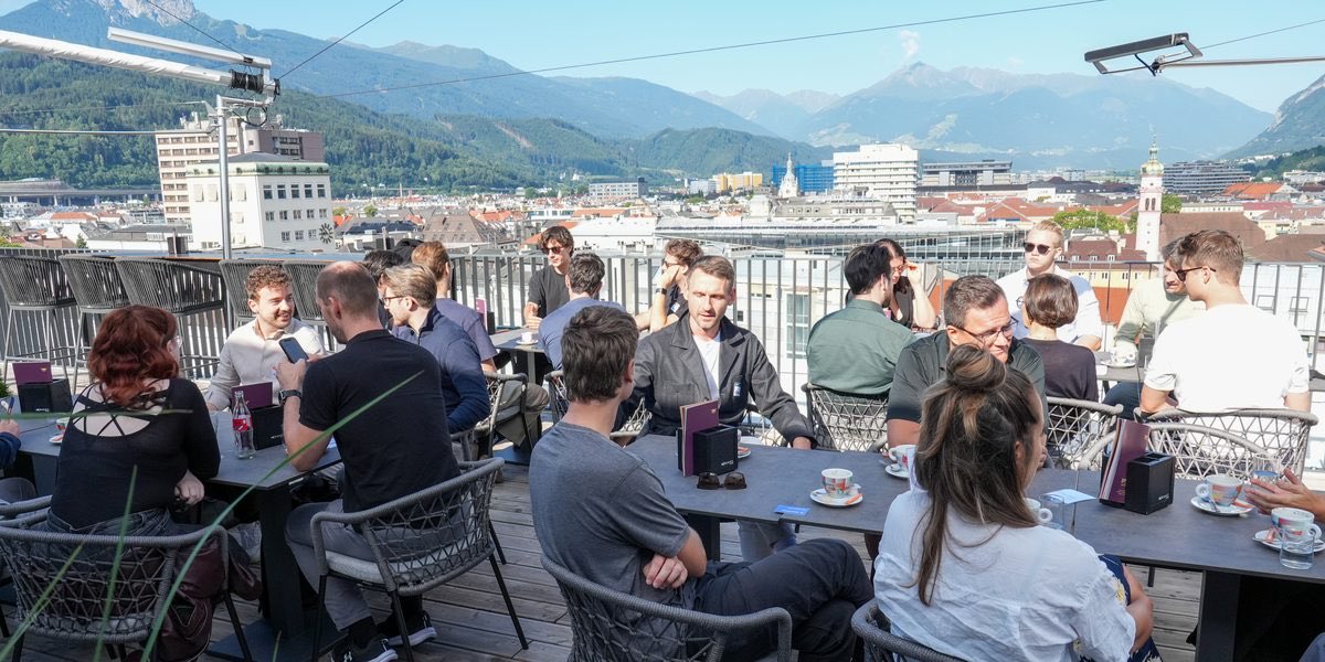 Drei besetzte Tische auf einer Dachterrasse über Innsbruck, alle im Gespräch, dahinter Altstadt und Nordkette
